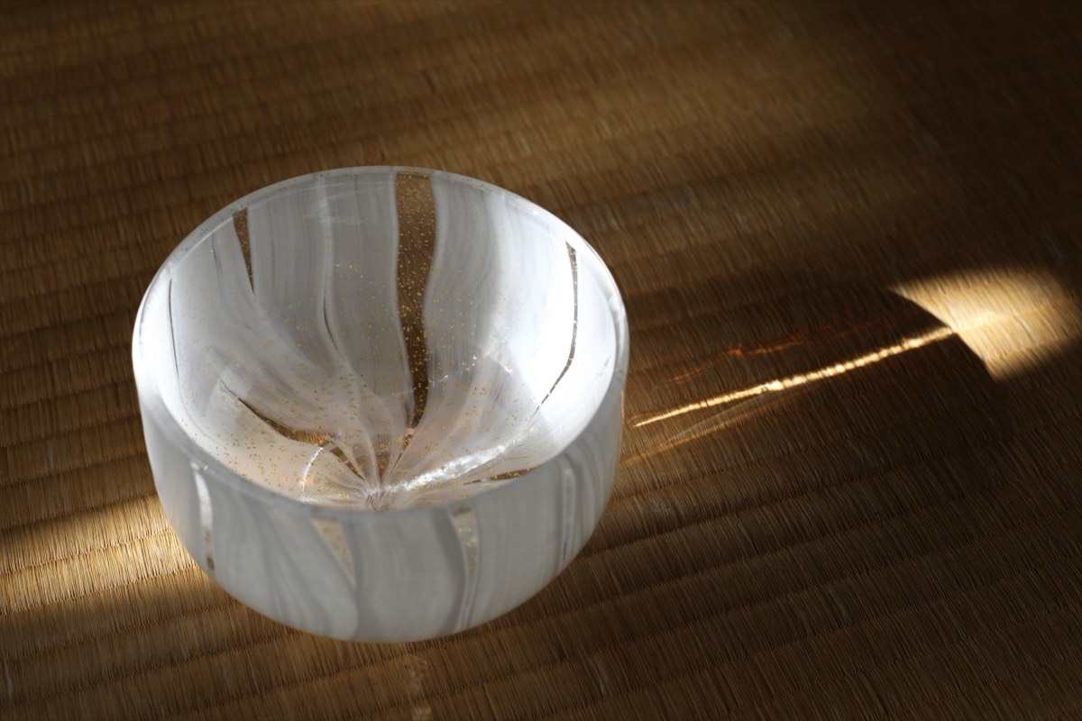 A glass tea bowl on tatami, lit by a narrow shaft of light falling across the mat.