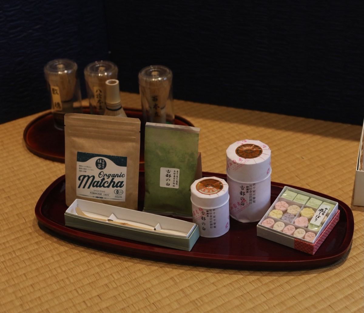 Matcha packets, tea canisters and a box of seasonal sweets arranged on a red lacquer tray.