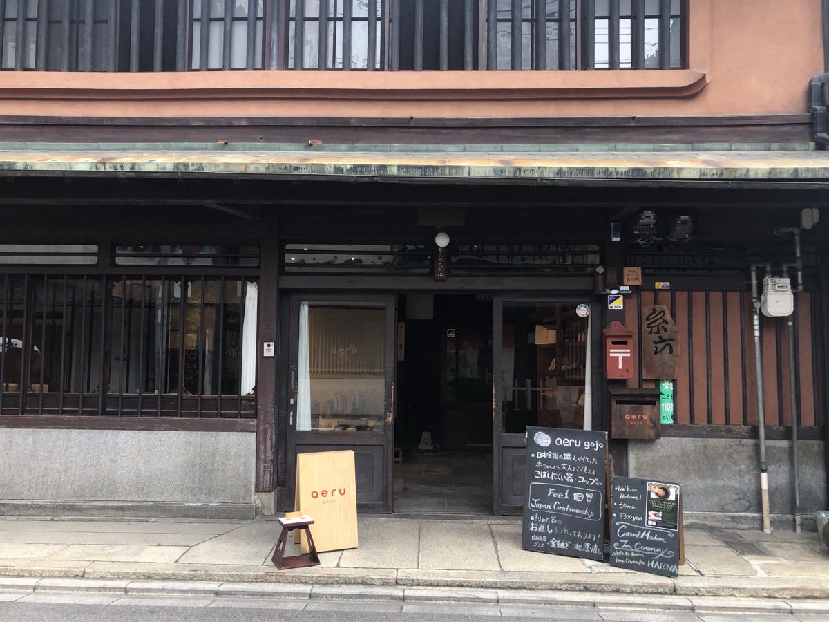 The street frontage of aeru gojo: a wooden machiya with lattice windows, an aeru sign board and a chalkboard by the open entrance.